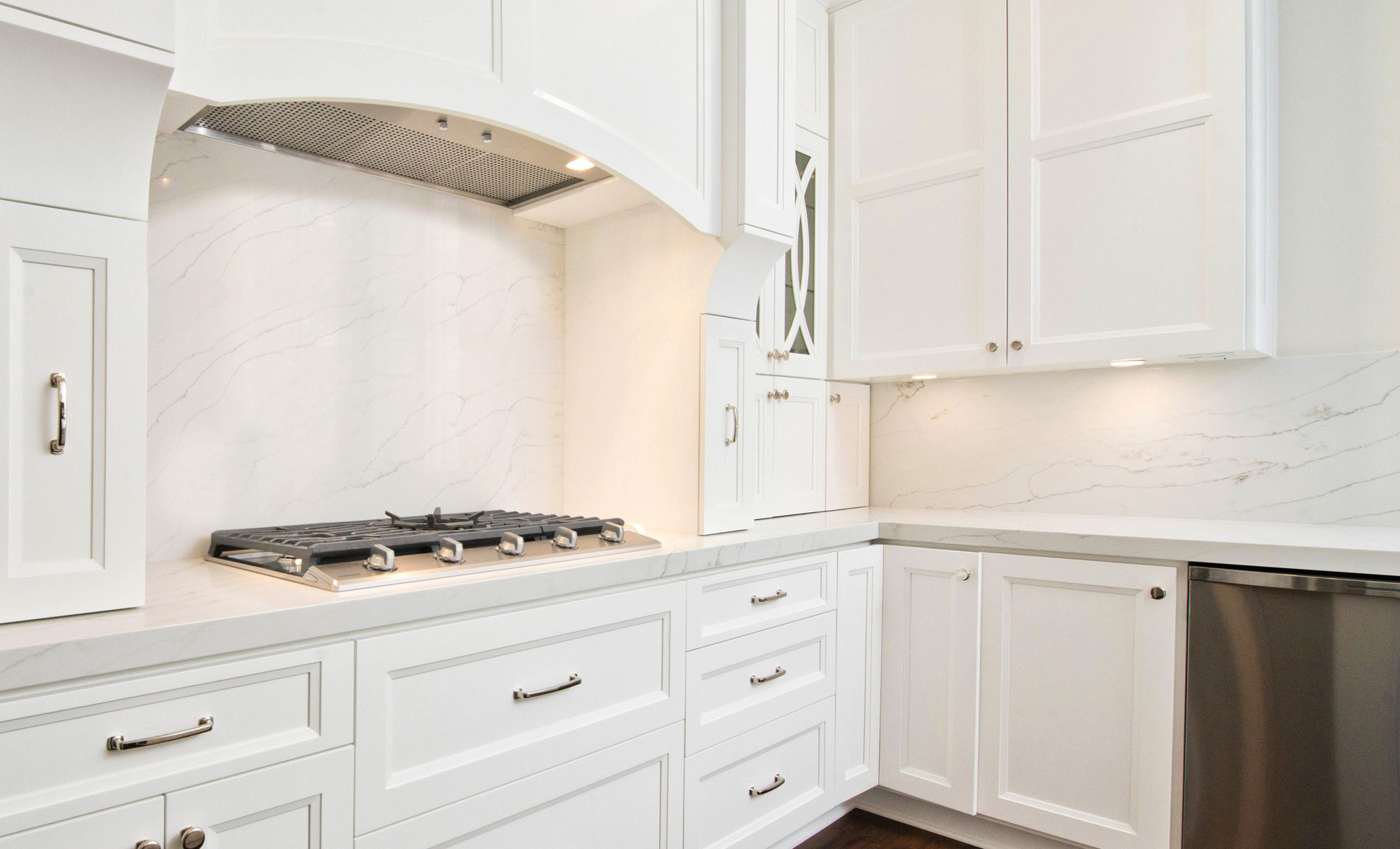 A contemporary kitchen countertop has minimal quartz veining. Custom white cabinetry maximizes the kitchen’s functionality.