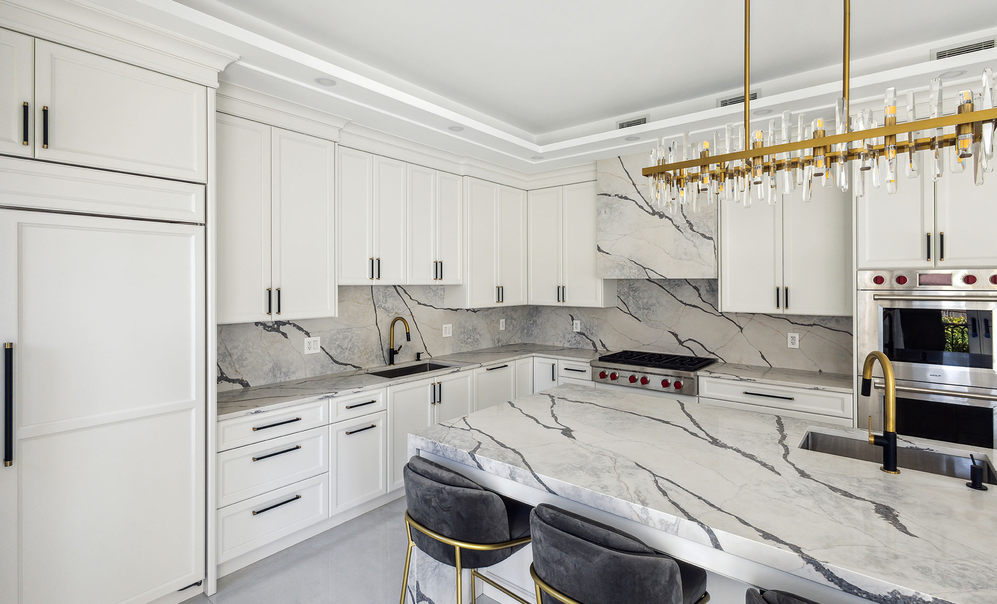 A quartz kitchen island and matching countertops have dramatic statement veining. They are set against minimal white cabinetry.
