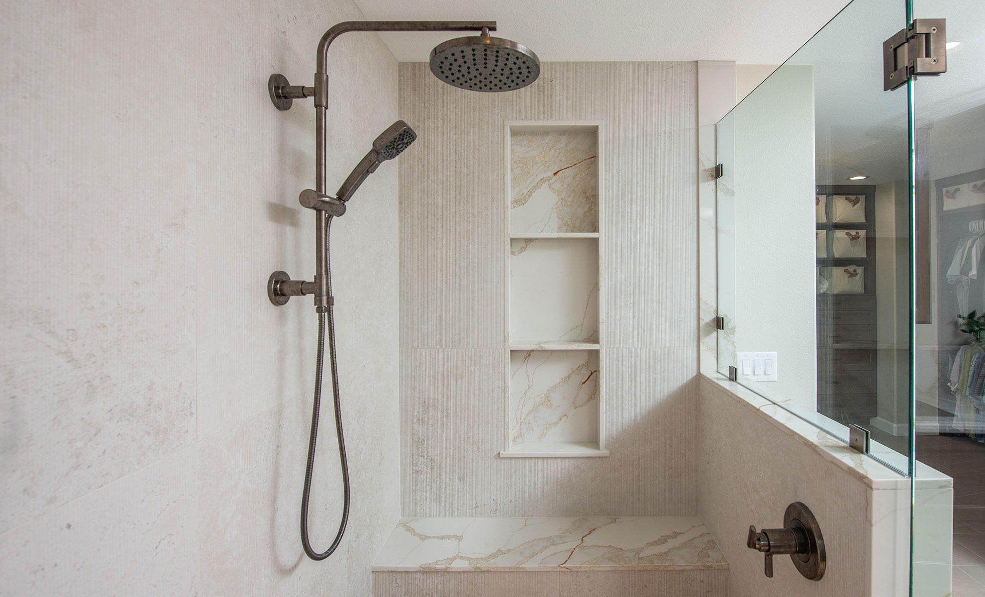 This image depicts a modern, spa-like bathroom featuring quartz surfaces and a waterfall shower.