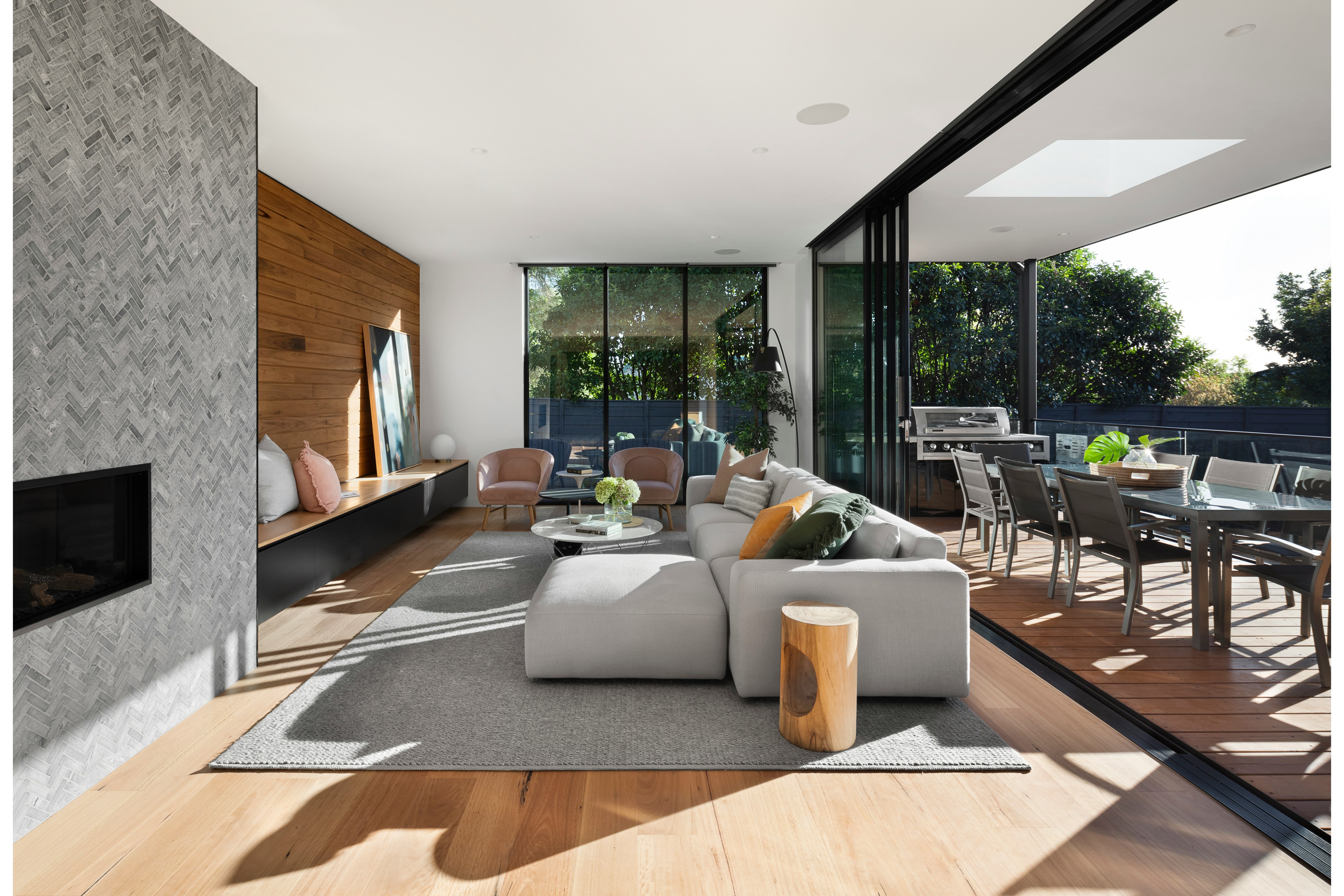 Modern living room with a gray sectional, fireplace, and open glass doors leading to an outdoor dining area.